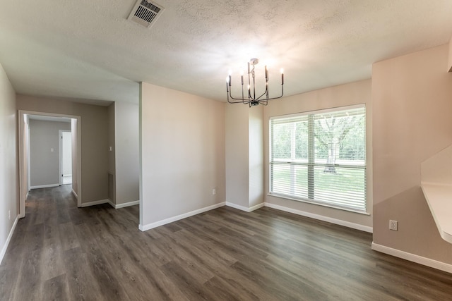 unfurnished dining area featuring dark wood-style flooring, a textured ceiling, a chandelier, baseboards, and visible vents