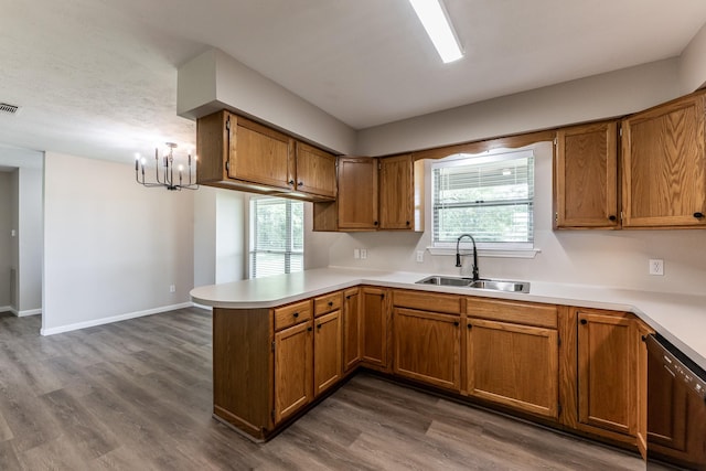 kitchen featuring a sink, an inviting chandelier, brown cabinetry, and a peninsula