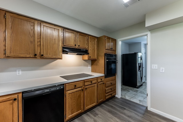 kitchen featuring brown cabinetry, visible vents, black appliances, dark wood-style floors, and under cabinet range hood