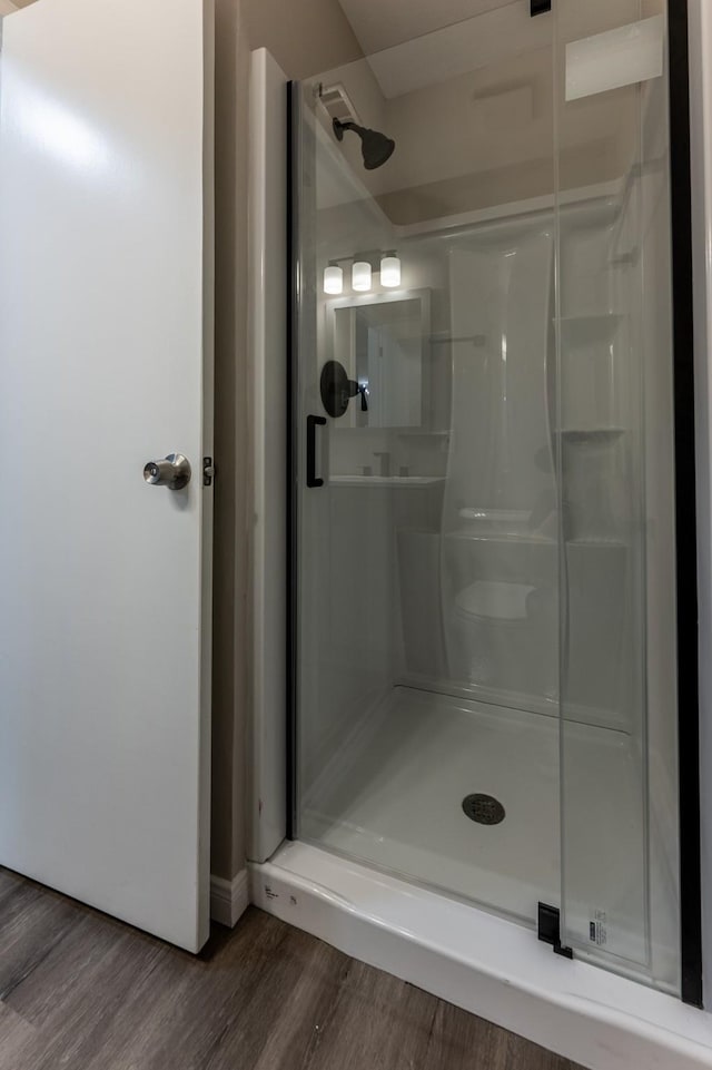 full bath with baseboards, a stall shower, and wood finished floors