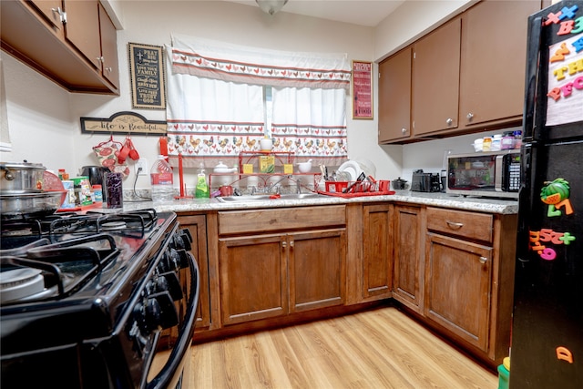 kitchen featuring light wood-style floors, light countertops, brown cabinetry, and black appliances