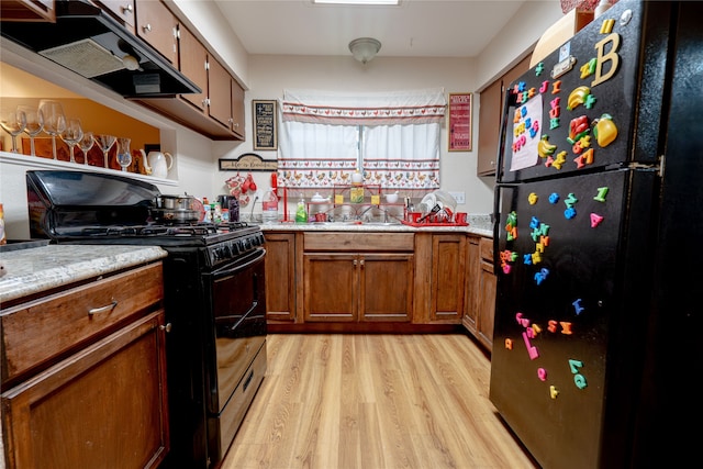 kitchen featuring brown cabinets, a sink, light wood finished floors, under cabinet range hood, and black appliances