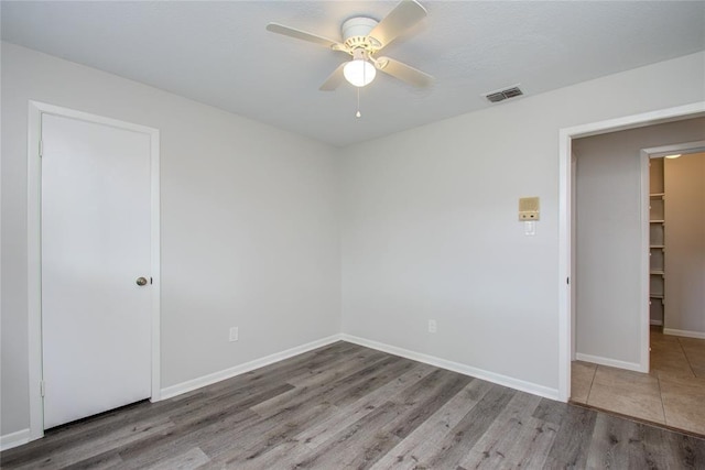 empty room with baseboards, ceiling fan, visible vents, and wood finished floors