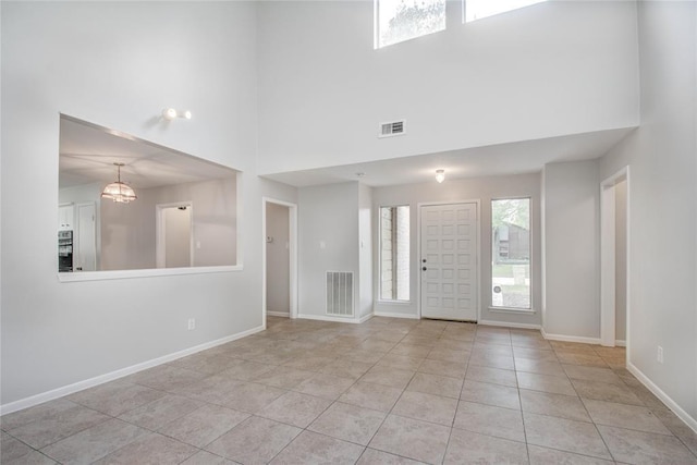 foyer featuring visible vents, a towering ceiling, baseboards, tile patterned floors, and a notable chandelier