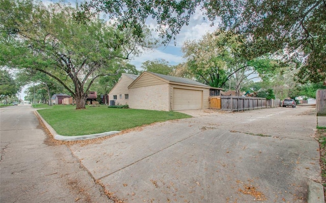 view of side of property featuring fence, an attached garage, brick siding, concrete driveway, and a yard