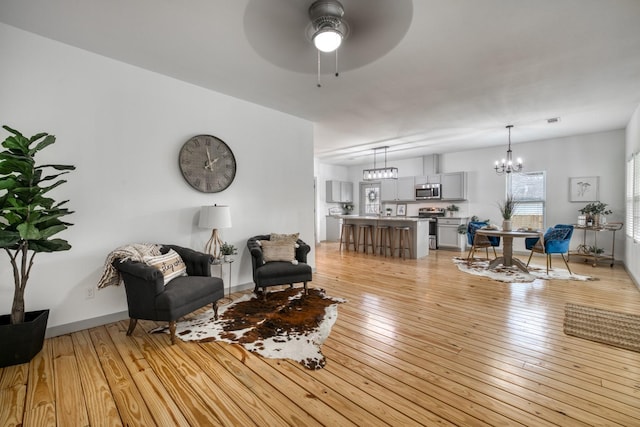 living room featuring ceiling fan with notable chandelier and light wood-style flooring