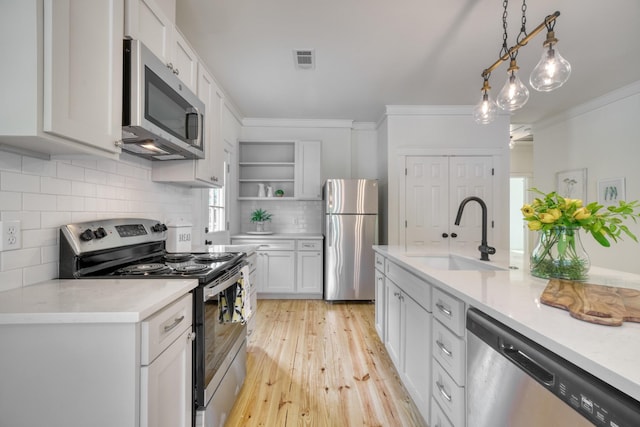 kitchen with crown molding, open shelves, appliances with stainless steel finishes, a sink, and light wood-style flooring
