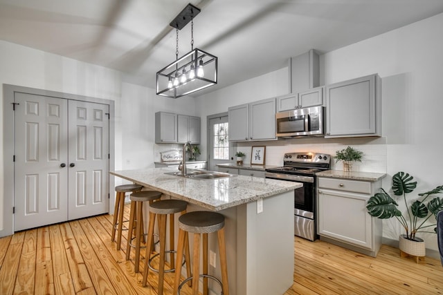 kitchen with gray cabinets, decorative backsplash, appliances with stainless steel finishes, a sink, and light wood finished floors