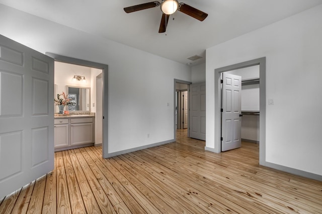 unfurnished bedroom featuring light wood-style floors, baseboards, ensuite bathroom, a walk in closet, and ceiling fan
