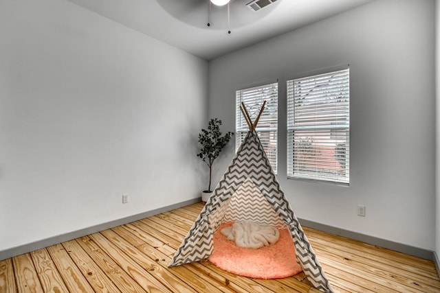 recreation room with baseboards, ceiling fan, wood finished floors, and visible vents