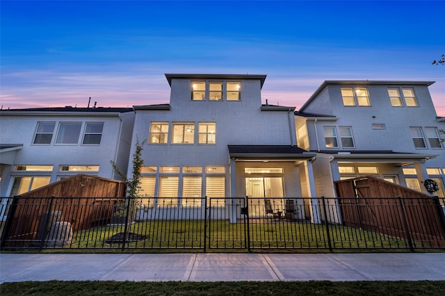 back of house at dusk featuring a fenced front yard, a yard, and stucco siding