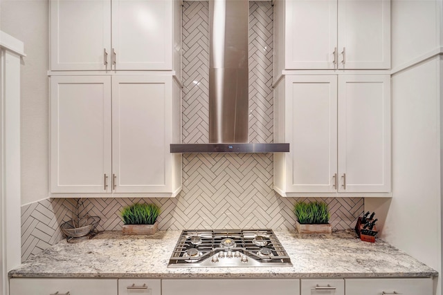 kitchen with wall chimney range hood, decorative backsplash, light stone countertops, white cabinets, and stainless steel gas stovetop