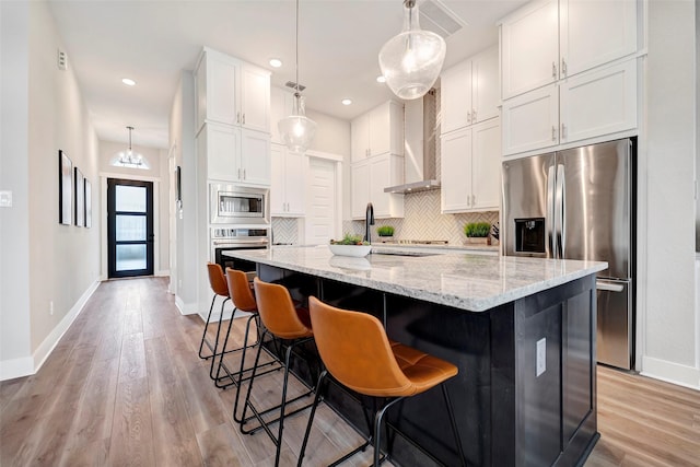 kitchen featuring baseboards, wall chimney range hood, white cabinetry, tasteful backsplash, and stainless steel appliances
