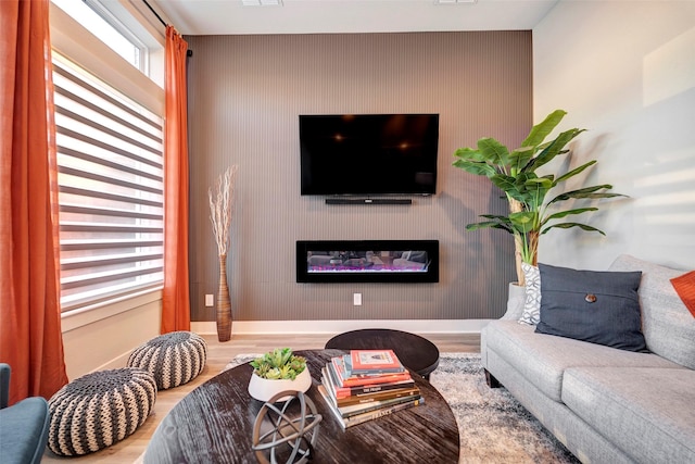 living room featuring baseboards, a glass covered fireplace, wood finished floors, and an accent wall