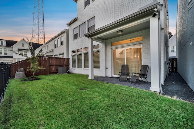 rear view of property with central AC, brick siding, a fenced backyard, a lawn, and a patio