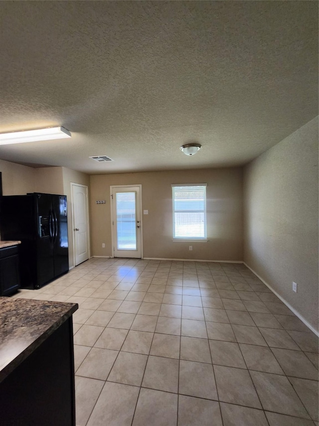 interior space featuring light tile patterned floors, baseboards, a textured ceiling, and black refrigerator with ice dispenser