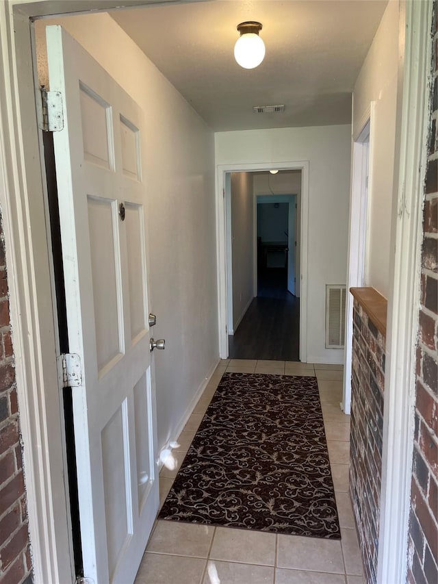 hall featuring light tile patterned floors and brick wall