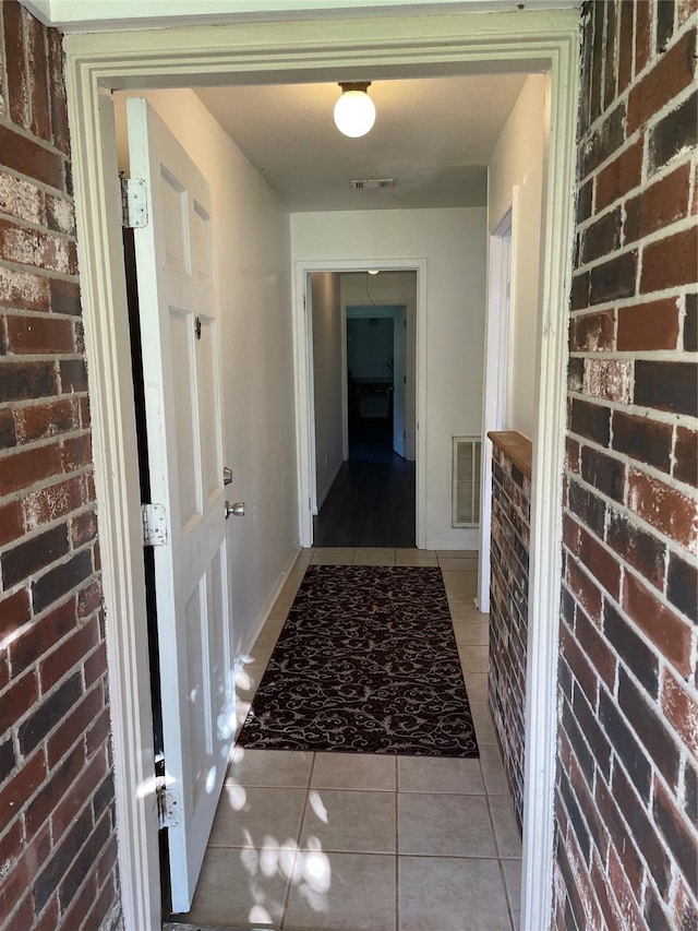 corridor with light tile patterned floors, brick wall, and baseboards
