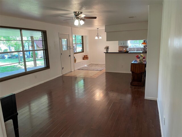 unfurnished living room with a ceiling fan, baseboards, and dark wood-style floors