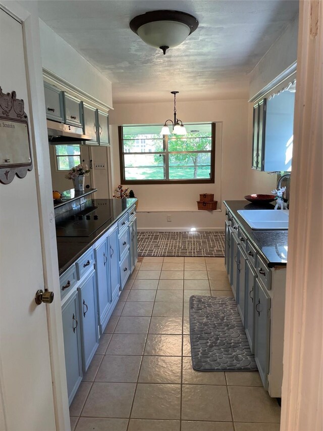 kitchen featuring dark countertops, a sink, light tile patterned floors, under cabinet range hood, and hanging light fixtures