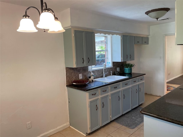 kitchen with a sink, tasteful backsplash, light tile patterned flooring, hanging light fixtures, and baseboards