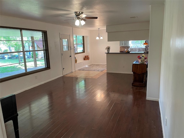 unfurnished living room with a ceiling fan, baseboards, and dark wood-style floors