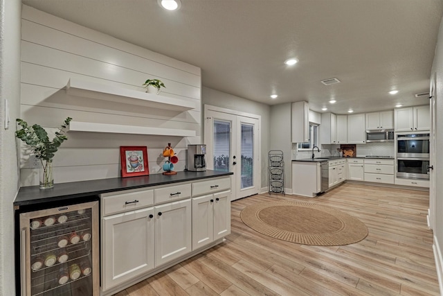 kitchen featuring wine cooler, stainless steel appliances, a sink, light wood-type flooring, and dark countertops