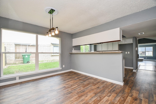 kitchen with a peninsula, a textured ceiling, dark wood-style flooring, hanging light fixtures, and baseboards