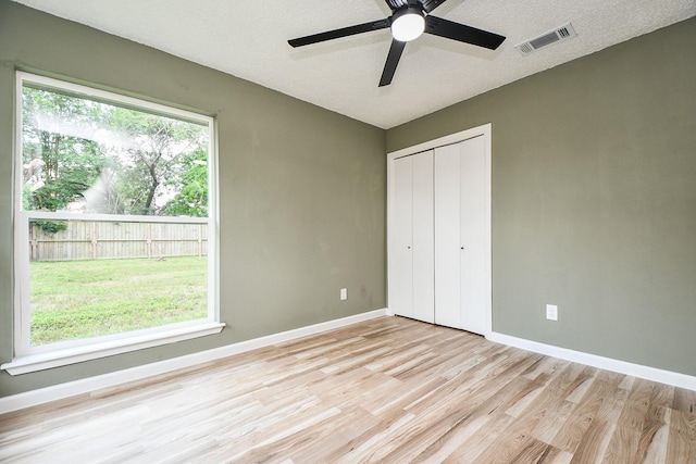 unfurnished bedroom with light wood finished floors, a closet, a textured ceiling, visible vents, and baseboards