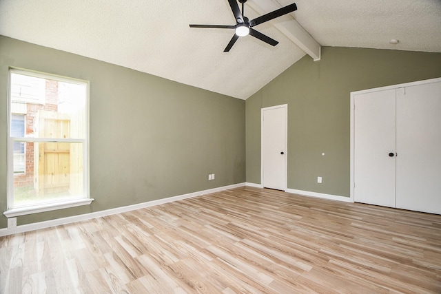 unfurnished bedroom with two closets, baseboards, vaulted ceiling with beams, and light wood-style floors
