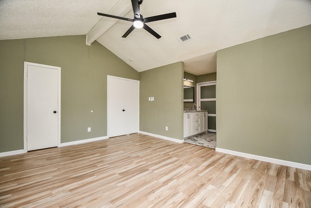 unfurnished living room featuring a sink, visible vents, light wood finished floors, a ceiling fan, and vaulted ceiling with beams