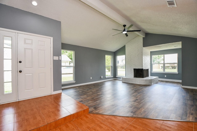 unfurnished living room featuring a brick fireplace, visible vents, wood finished floors, and ceiling fan