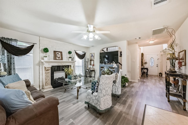 living room featuring wood finished floors, a ceiling fan, a large fireplace, and arched walkways