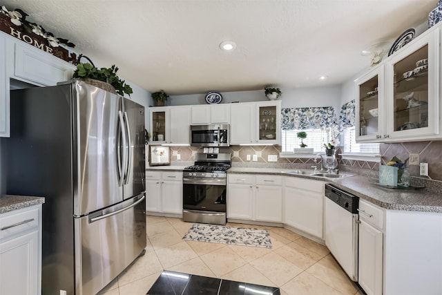 kitchen with appliances with stainless steel finishes, a sink, decorative backsplash, white cabinetry, and glass insert cabinets