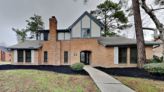 tudor house featuring roof with shingles, a chimney, and brick siding