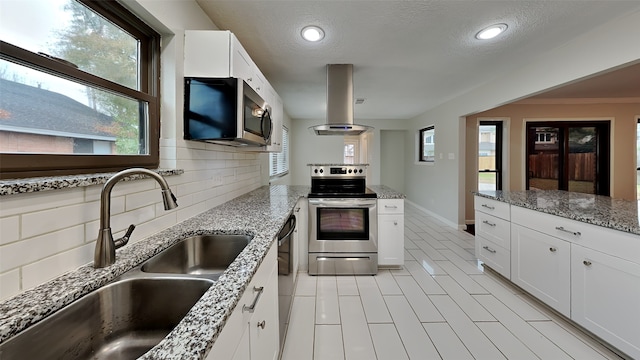 kitchen featuring island range hood, appliances with stainless steel finishes, tasteful backsplash, a sink, and a peninsula
