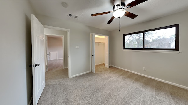 unfurnished bedroom with a walk in closet, light colored carpet, visible vents, baseboards, and a closet