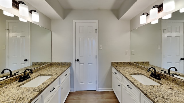 full bathroom with a sink, baseboards, wood finished floors, and two vanities