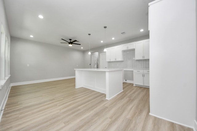 kitchen with white cabinets, a sink, a ceiling fan, open floor plan, and backsplash