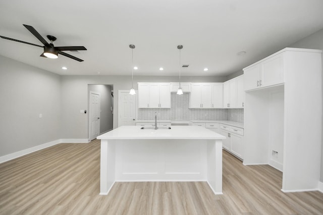 kitchen featuring a sink, ceiling fan, light wood-style floors, and a center island with sink