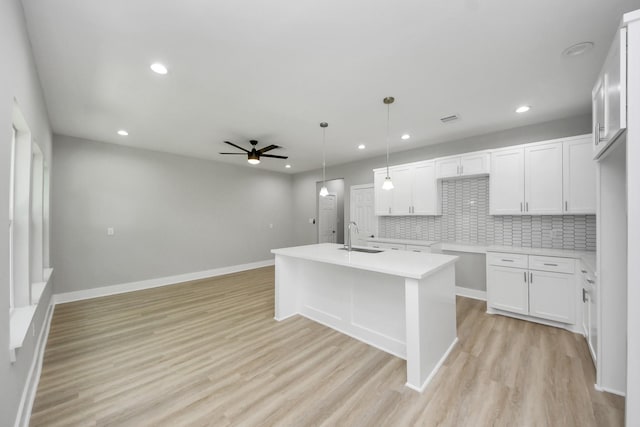 kitchen with a ceiling fan, open floor plan, tasteful backsplash, a sink, and light wood finished floors