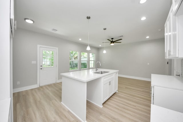 kitchen with a sink, a kitchen island with sink, light wood-style flooring, a ceiling fan, and white cabinetry