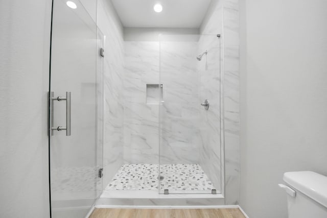 bathroom featuring wood finished floors, toilet, baseboards, recessed lighting, and a marble finish shower