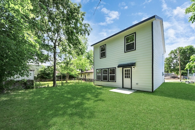 rear view of property featuring a lawn and fence
