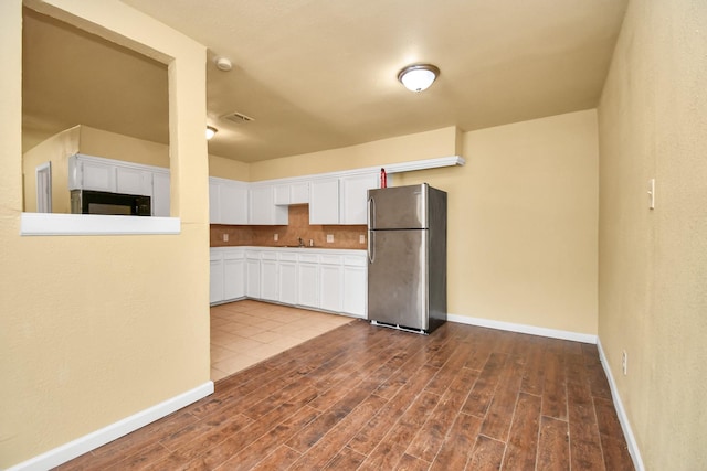 kitchen with freestanding refrigerator, black microwave, baseboards, dark wood-style floors, and white cabinetry