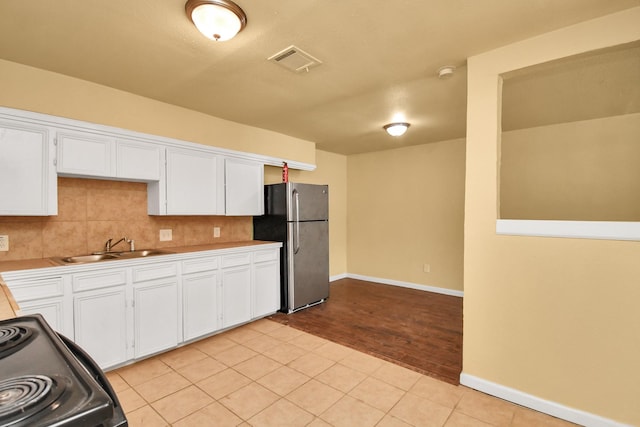 kitchen featuring visible vents, black electric range, a sink, freestanding refrigerator, and white cabinetry