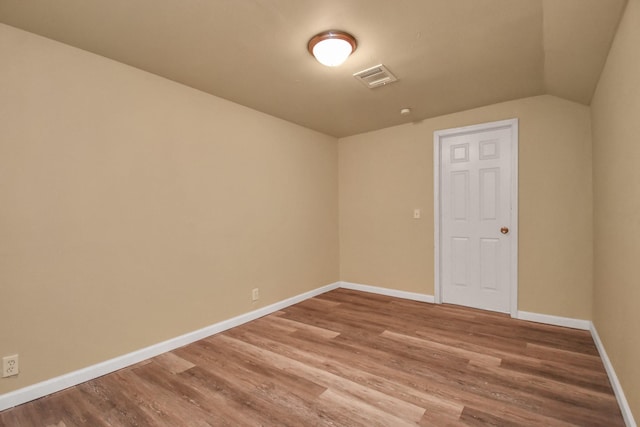 empty room with baseboards, visible vents, wood finished floors, and vaulted ceiling