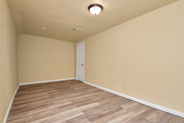unfurnished room featuring baseboards, vaulted ceiling, wood finished floors, and visible vents