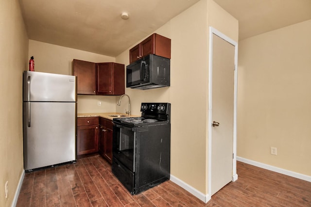 kitchen featuring dark wood-style flooring, a sink, light countertops, baseboards, and black appliances