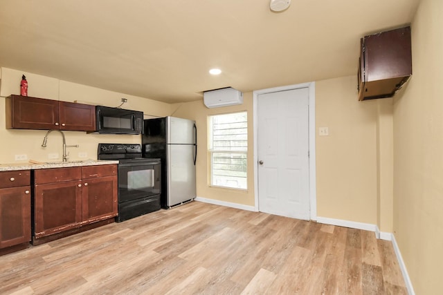 kitchen featuring a sink, baseboards, a wall unit AC, light wood-type flooring, and black appliances